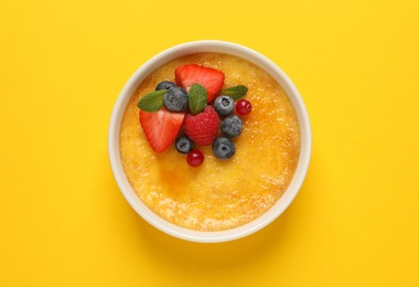Photo of Delicious creme brulee with fresh berries on yellow background, top view