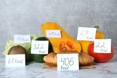 Photo of Food products with calorific value tags on white marble table. Weight loss concept