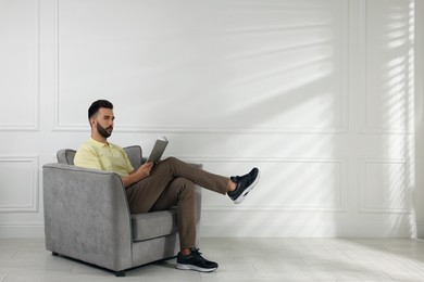 Photo of Man reading book in armchair near white wall, space for text