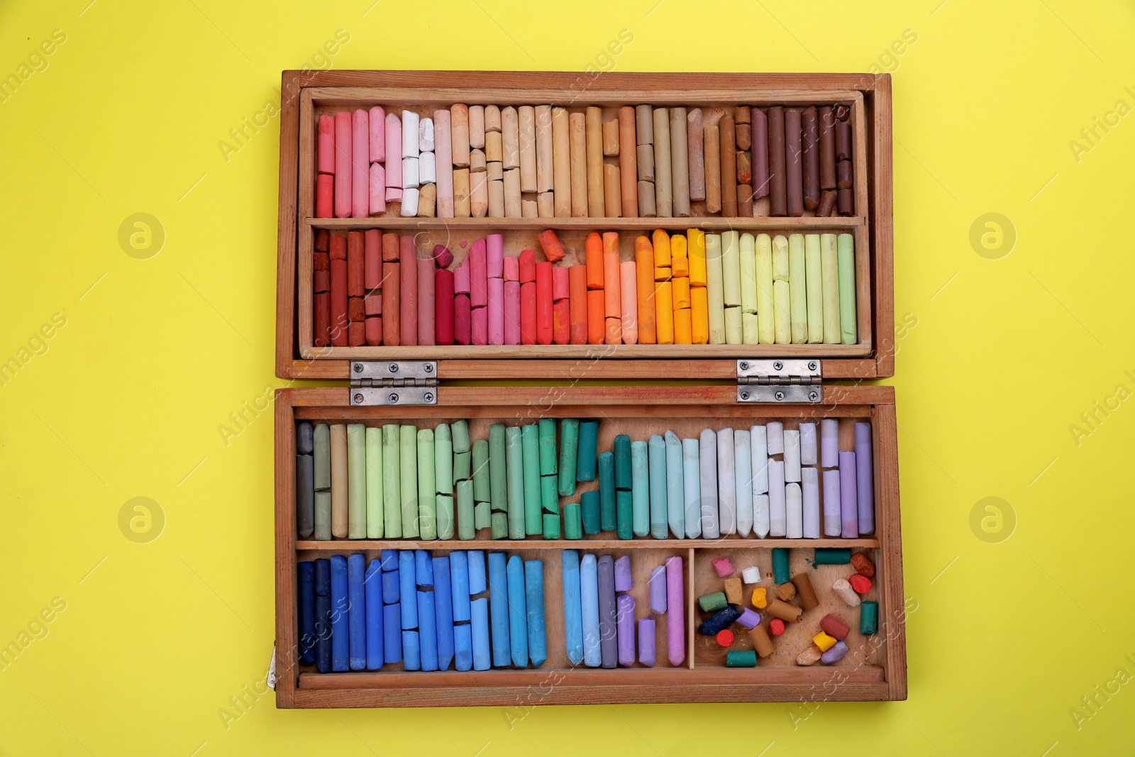 Photo of Set of soft pastels in wooden box on yellow background, top view. Drawing material