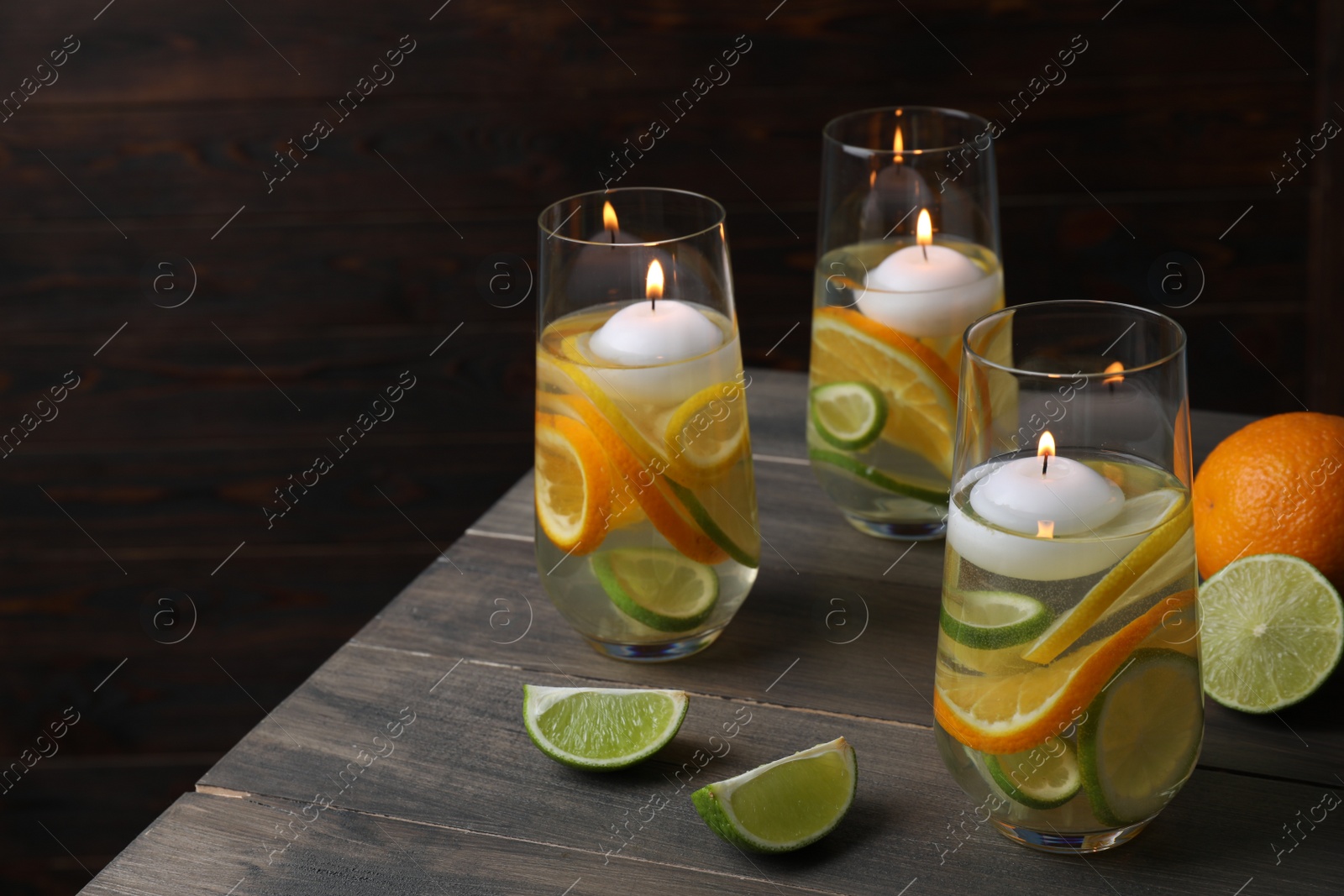 Photo of Candles and fruit slices in glass holders with liquid on wooden table