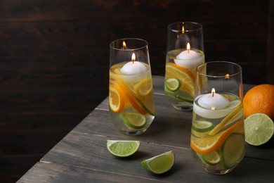 Candles and fruit slices in glass holders with liquid on wooden table