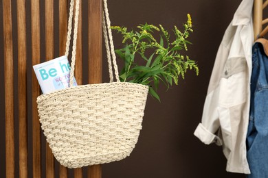 Photo of Stylish beach bag with plant and magazine hanging indoors. Space for text