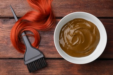 Photo of Henna cream, brush and red strand on wooden table, flat lay. Natural hair coloring