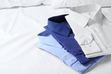 Photo of Stylish folded shirts on bed. Dry-cleaning service