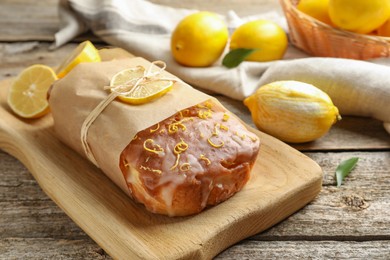 Photo of Wrapped tasty lemon cake with glaze and citrus fruits on wooden table