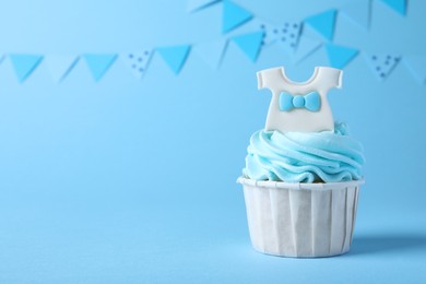 Beautifully decorated baby shower cupcake with cream and boy topper on light blue background. Space for text