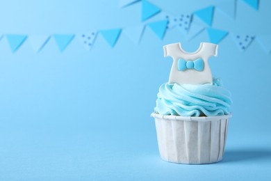 Photo of Beautifully decorated baby shower cupcake with cream and boy topper on light blue background. Space for text