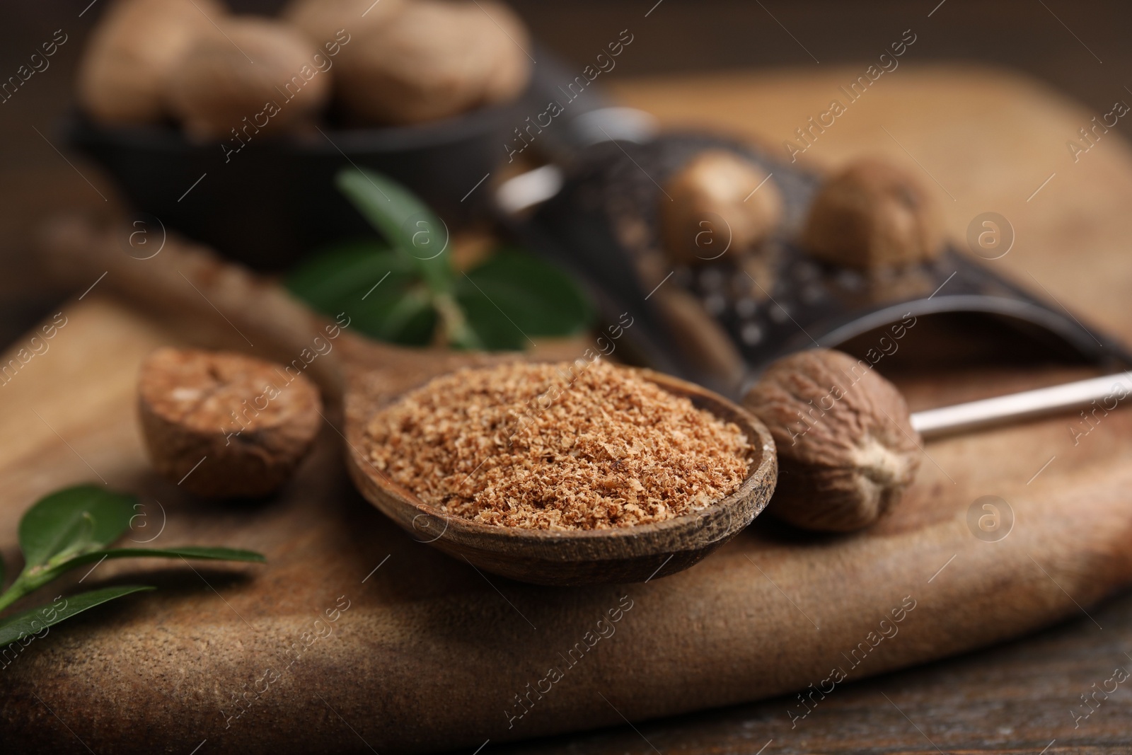 Photo of Spoon with grated nutmeg on wooden board, closeup