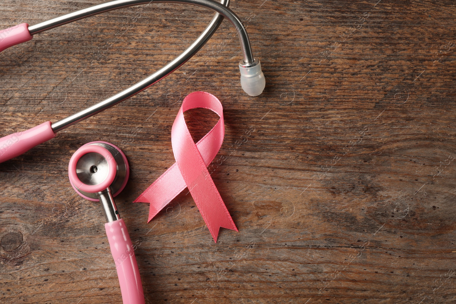 Photo of Pink ribbon and stethoscope on wooden background, top view with space for text. Breast cancer concept