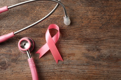 Pink ribbon and stethoscope on wooden background, top view with space for text. Breast cancer concept