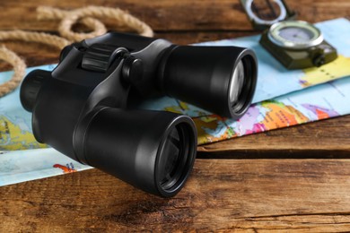 Modern binoculars, map, compass and rope on wooden table, closeup