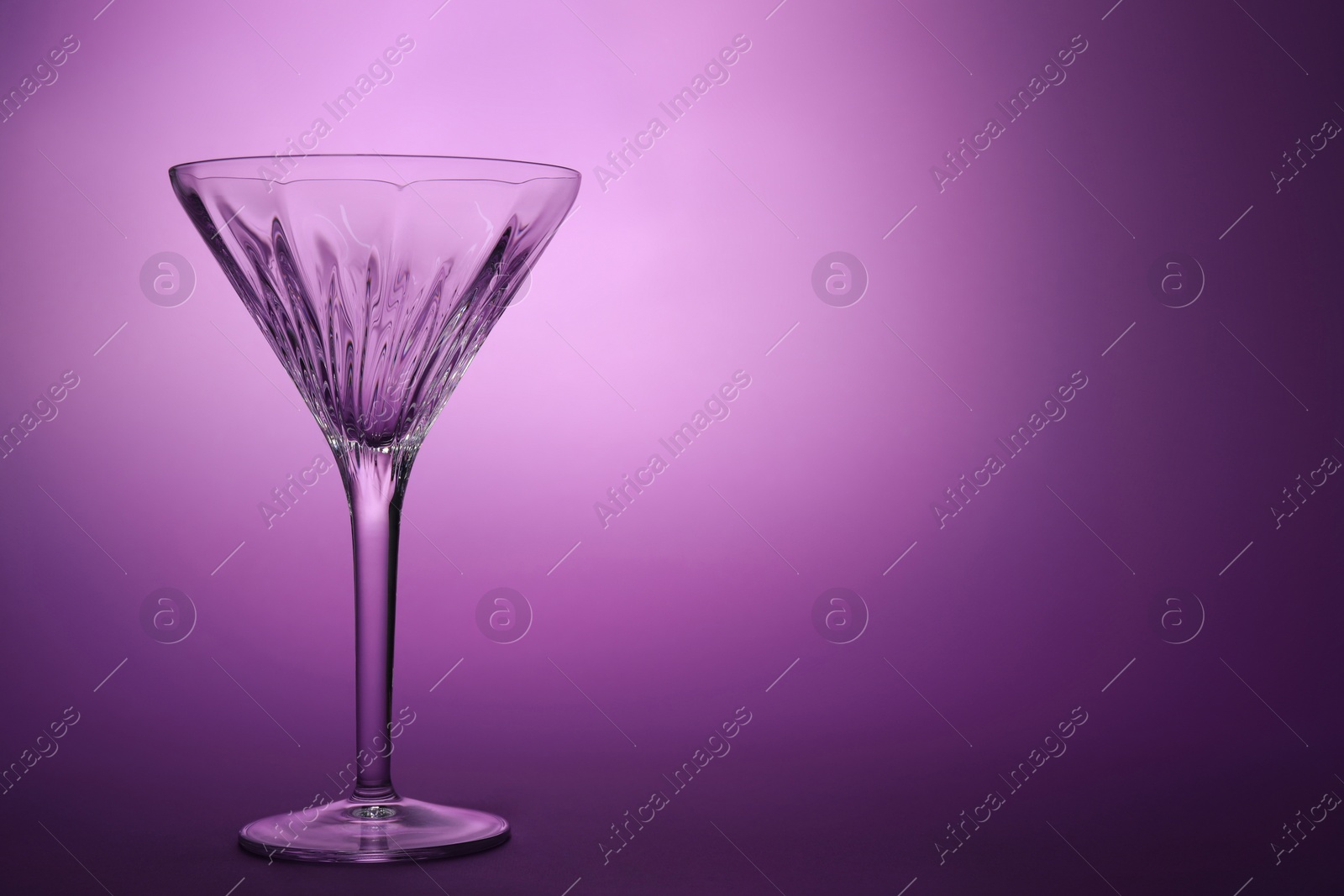 Photo of Elegant empty martini glass on purple background. Space for text