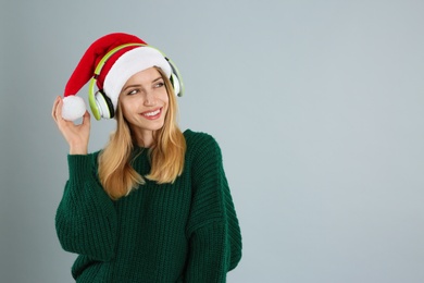 Photo of Happy woman with headphones on grey background, space for text. Christmas music