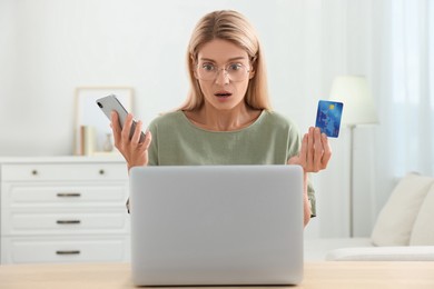 Photo of Stressed woman with credit card and smartphone using laptop at home. Be careful - fraud