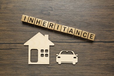 Photo of Word Inheritance made with cubes, cutouts of car and house on wooden table, flat lay