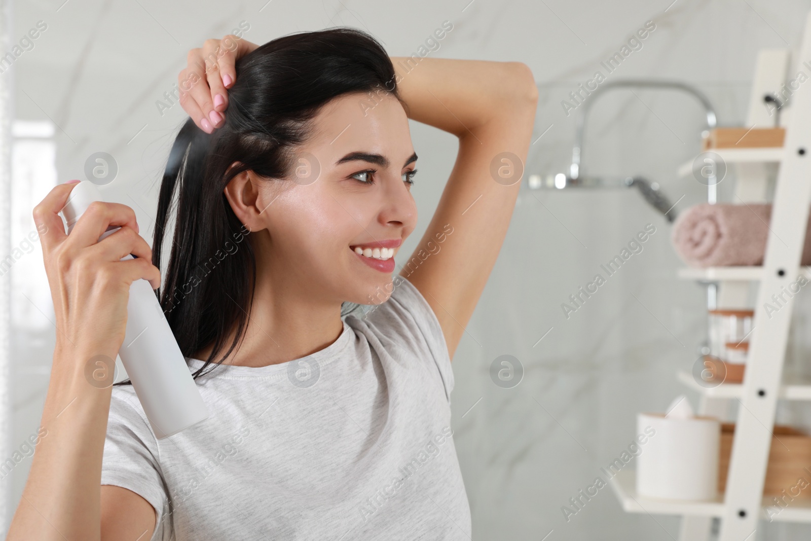 Photo of Woman applying dry shampoo onto her hair in bathroom