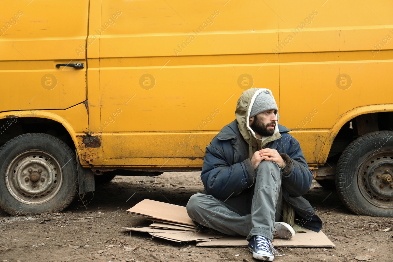 Photo of Poor homeless man sitting near van outdoors