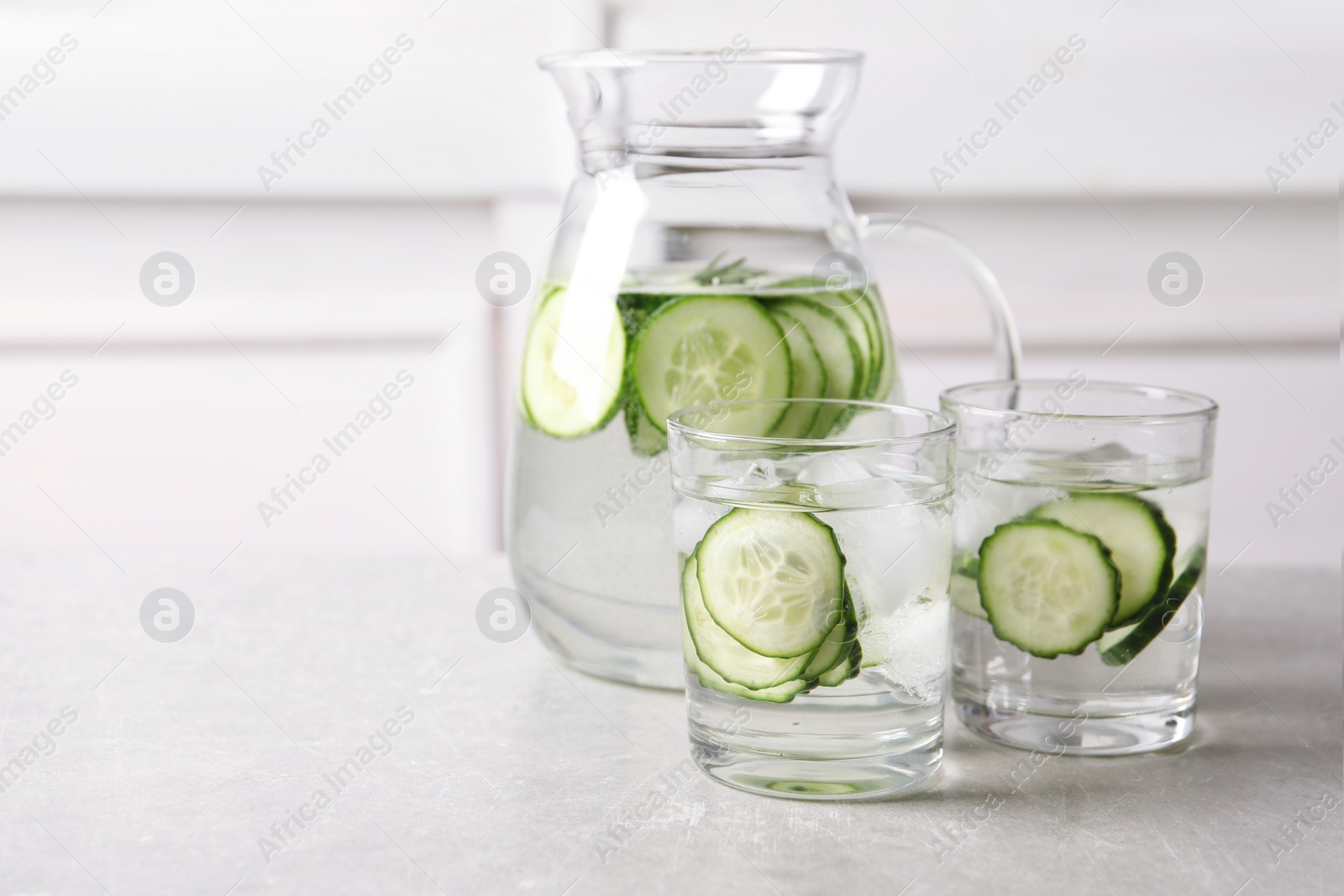 Photo of Glasses and jug of fresh cucumber water on table. Space for text