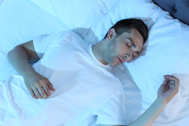 Photo of Young man sleeping in bed at night, top view