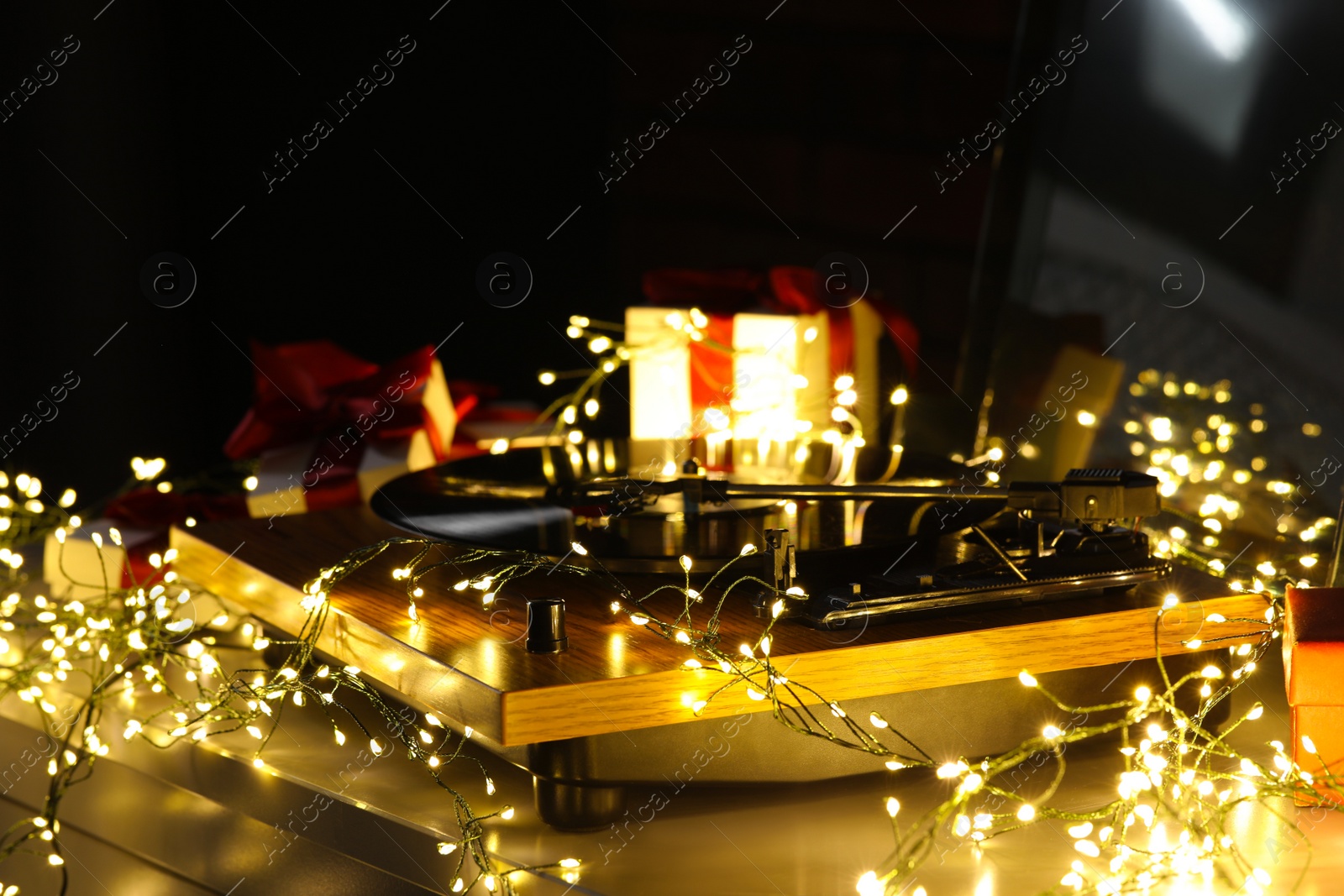 Photo of Turntable with vinyl record, fairy lights and Christmas gift boxes on grey table, closeup