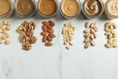 Photo of Tasty nut butters in jars and raw nuts on white marble table, flat lay. Space for text