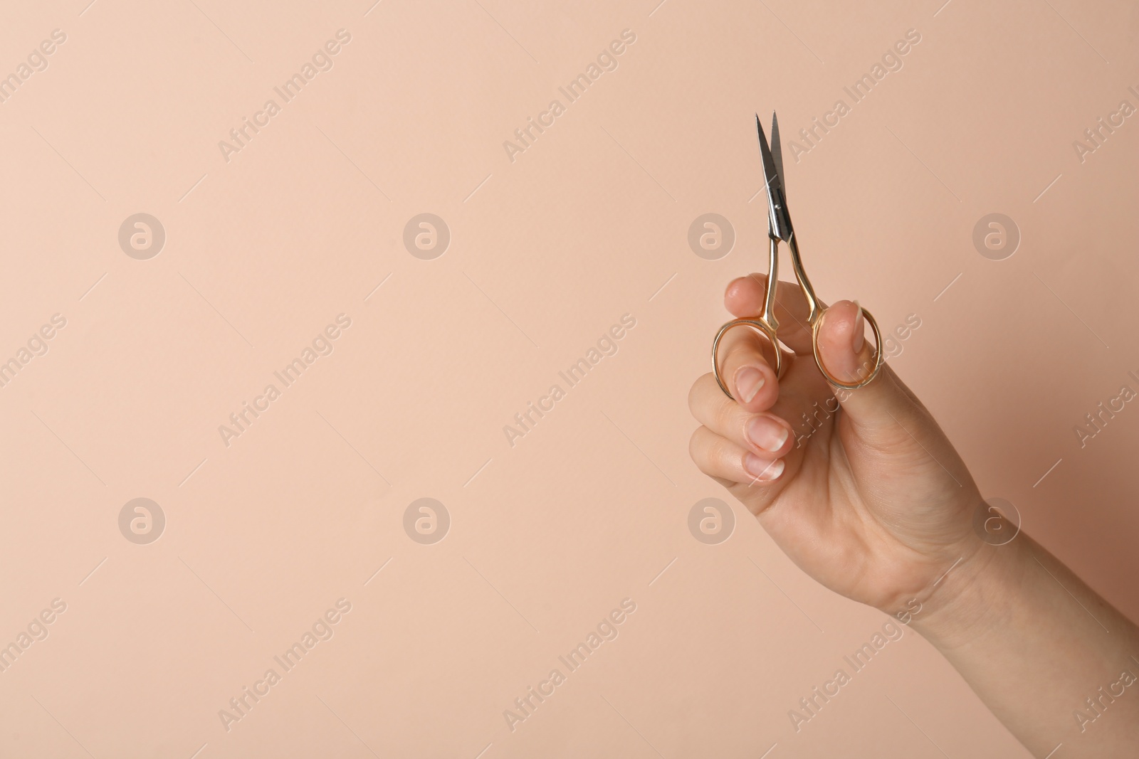 Photo of Woman holding sewing scissors on beige background, closeup. Space for text