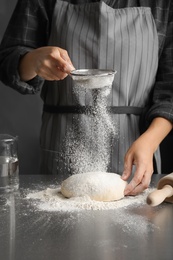 Woman sprinkling dough for pastry with flour on table
