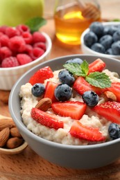 Photo of Tasty oatmeal porridge with berries and almond nuts in bowl served on wooden board