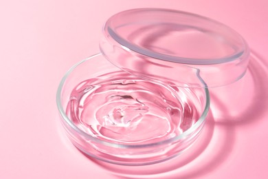 Photo of Petri dish with liquid and lid on pale pink background, closeup