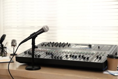 Photo of Microphone and professional mixing console on wooden table in radio studio