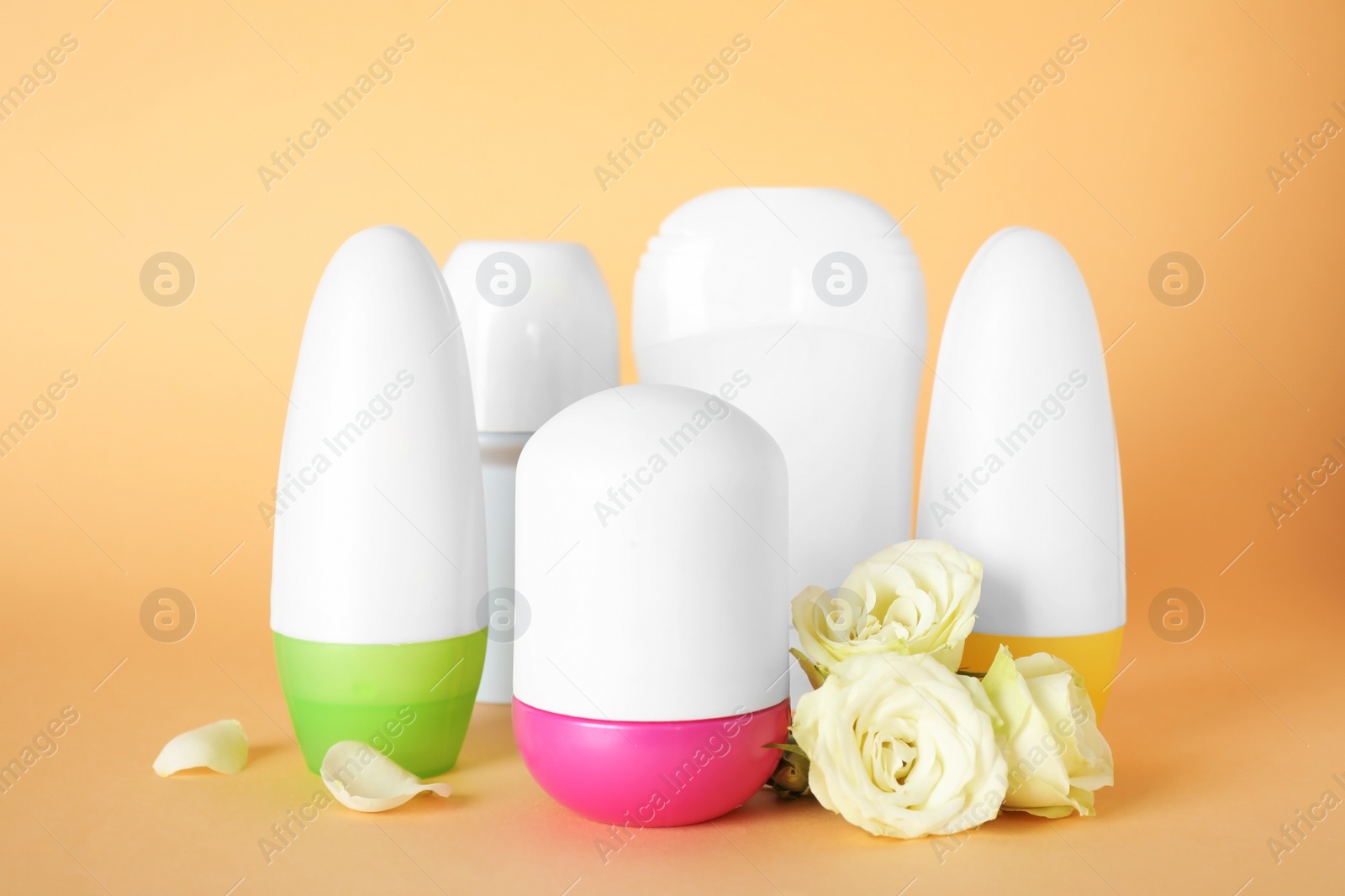 Photo of Different female deodorants and roses on light orange background