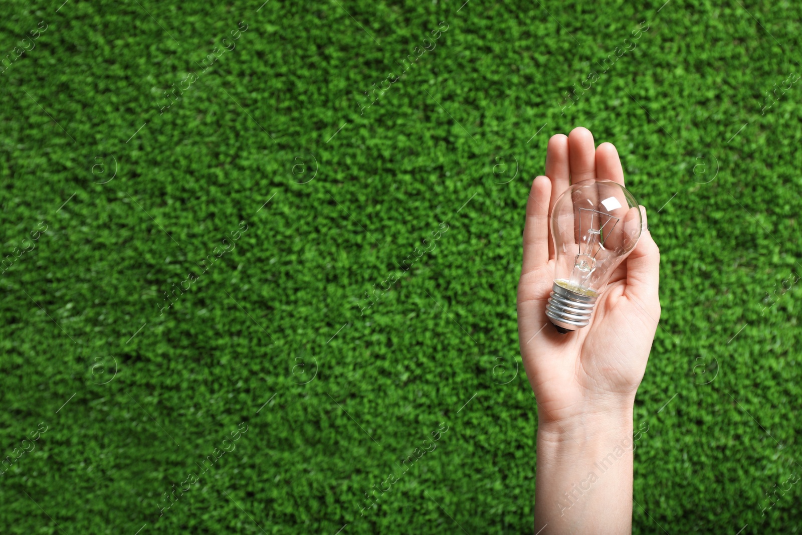 Photo of Woman holding incandescent light bulb over green grass, top view. Space for text