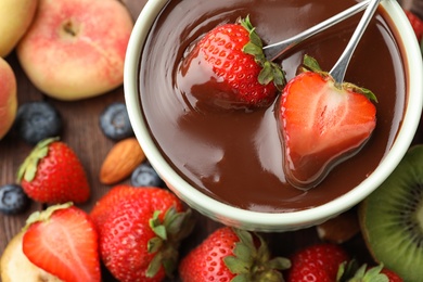 Photo of Fondue forks with strawberries in bowl of melted chocolate on table, flat lay