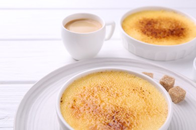 Photo of Delicious creme brulee in bowls, sugar cubes and coffee on white wooden table, closeup