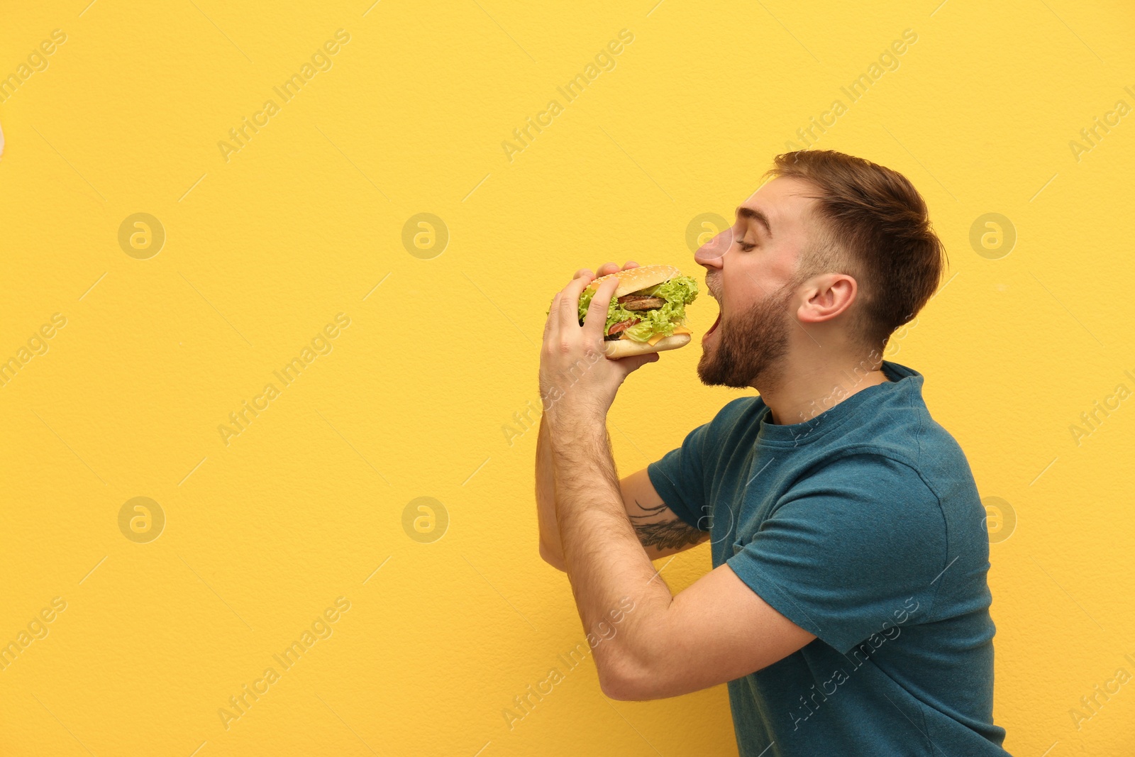 Photo of Young man eating tasty burger on color background. Space for text