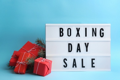 Photo of Lightbox with phrase BOXING DAY SALE and Christmas decorations on light blue background