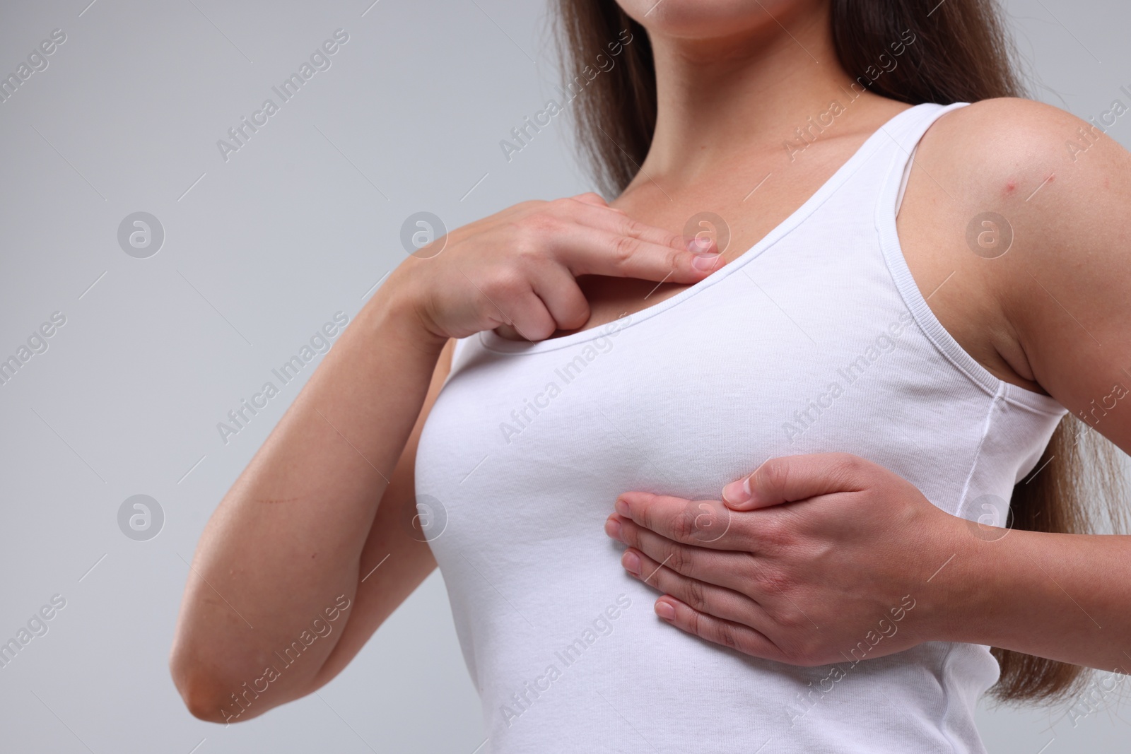 Photo of Woman doing breast self-examination on light grey background, closeup