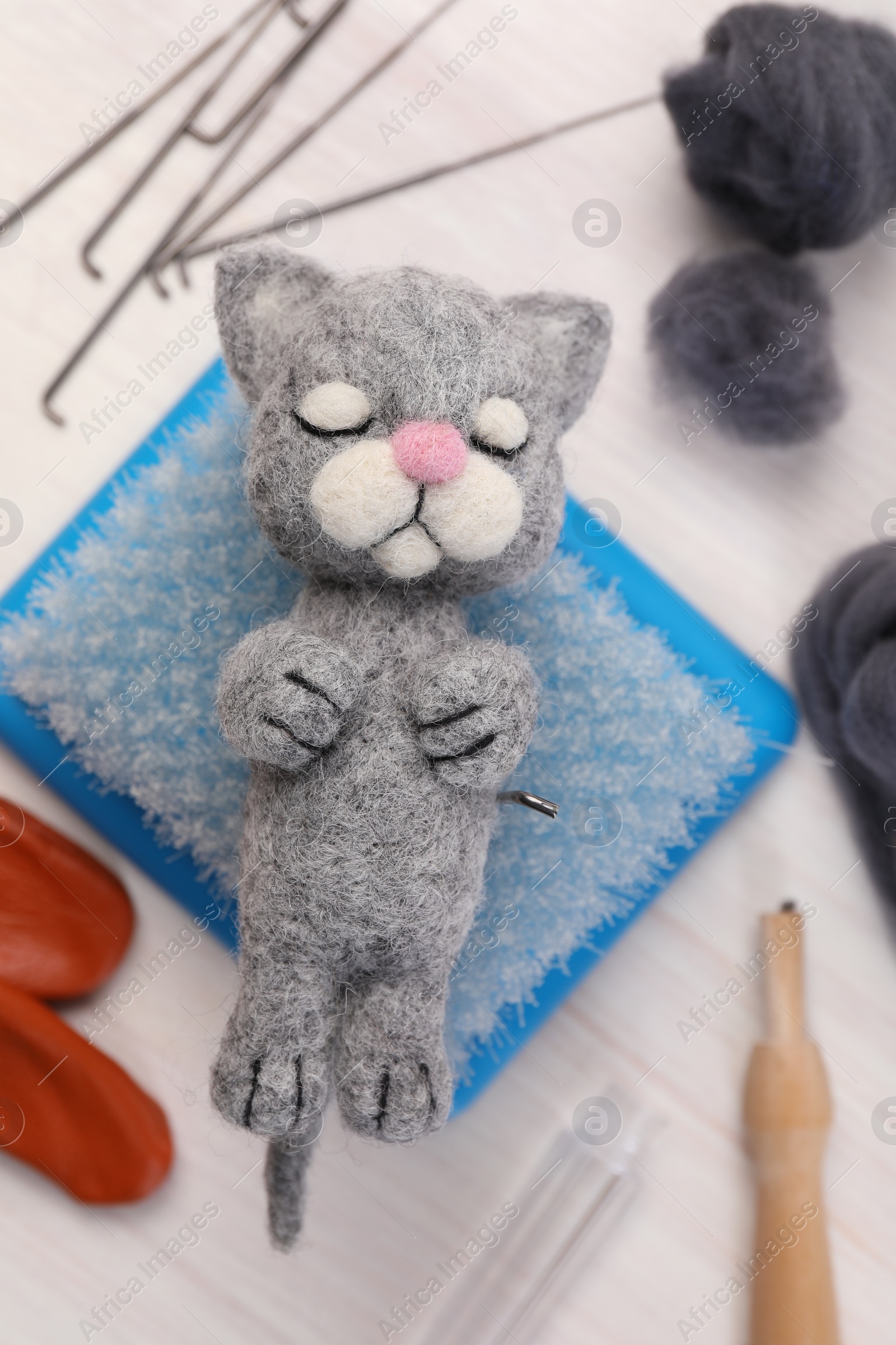 Photo of Felted cat, wool and different tools on light wooden table, flat lay