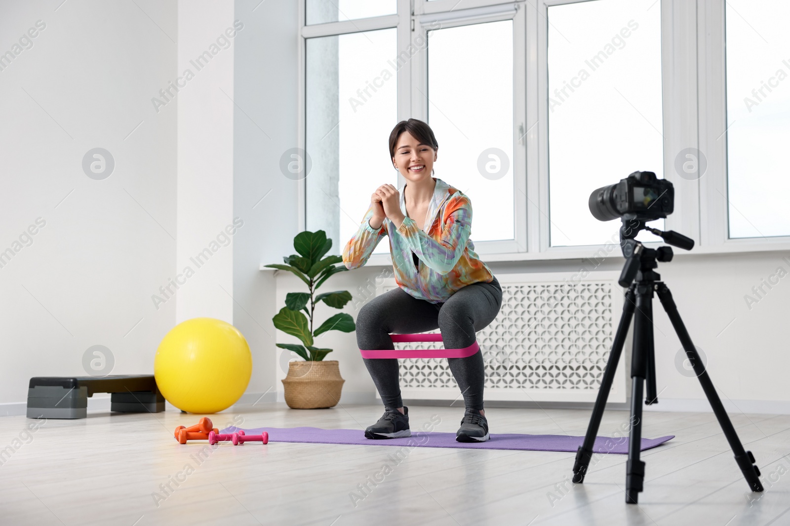 Photo of Happy sports blogger training with resistance band while recording fitness lesson at home