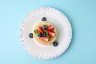 Delicious pancakes with strawberries, blueberries and mint on light blue background, top view