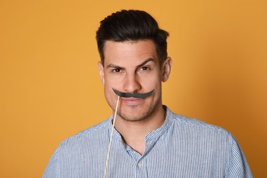 Funny man with fake mustache on yellow background