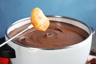 Photo of Dipping tangerine into pot with tasty chocolate fondue, closeup