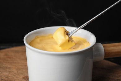 Photo of Pot of tasty cheese fondue and fork with bread on cutting board, closeup