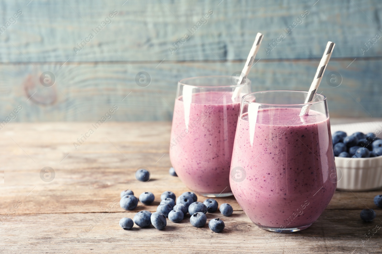 Photo of Tasty blueberry smoothie in glasses and berries on wooden table against color background with space for text