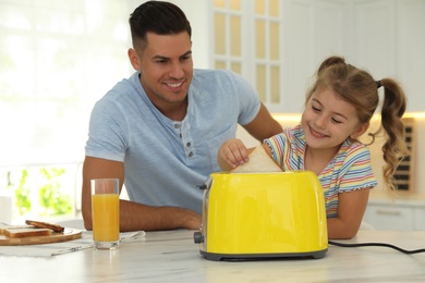 Photo of Father and daughter using toaster while having breakfast at table in kitchen