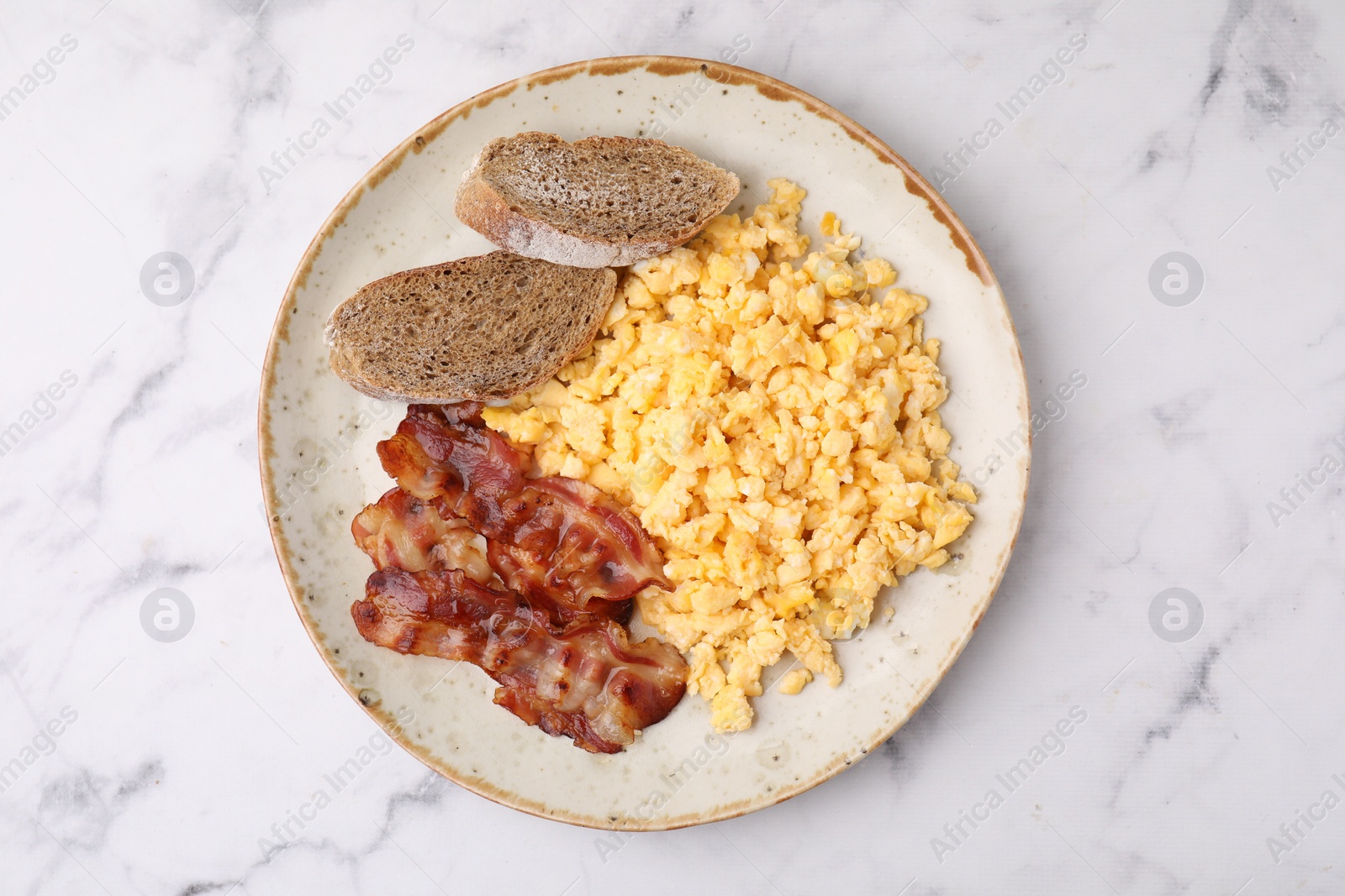 Photo of Delicious scrambled eggs with bacon in plate on white marble table, top view