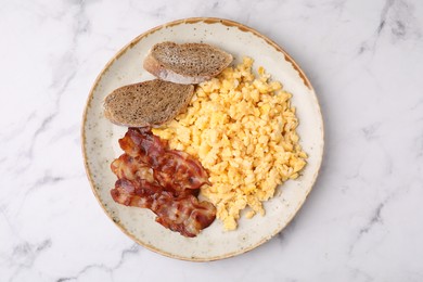 Delicious scrambled eggs with bacon in plate on white marble table, top view