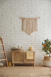 Stylish room interior with wooden cabinet and potted kumquat tree near white brick wall