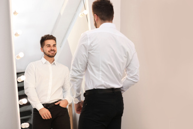 Young man looking at himself in large mirror at home